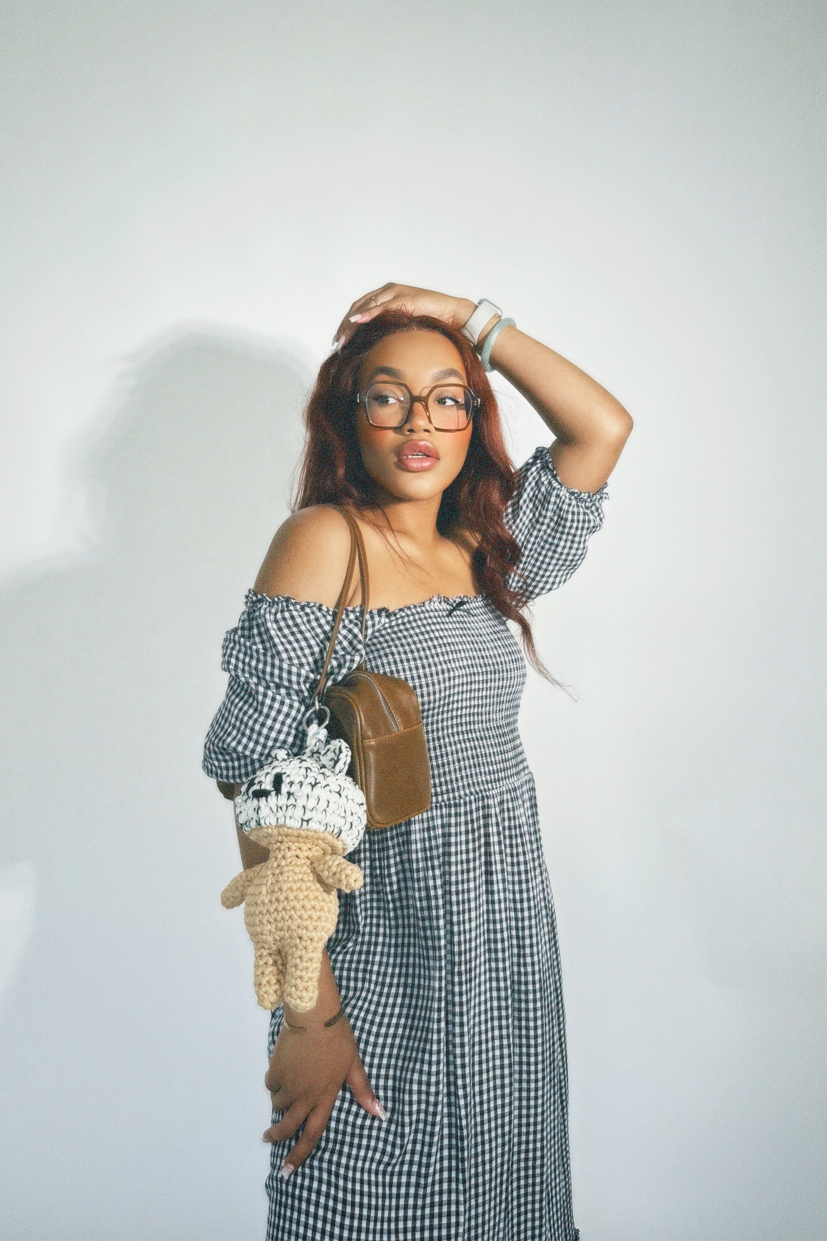 Woman in a checkered dress holding a small crocheted bag against a plain background